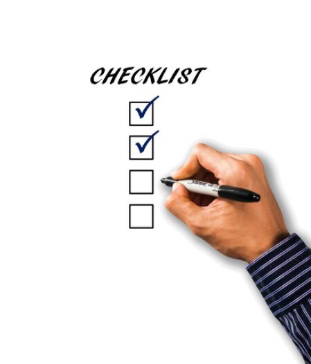 Checkliste mit Stift neben Telefon und E-Mail Symbolen